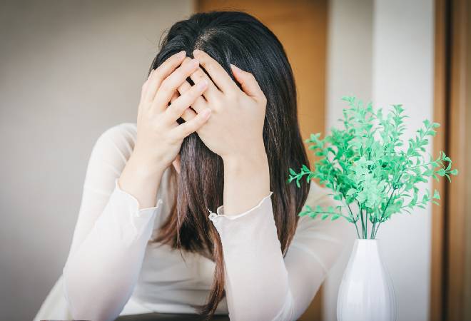 顏を手で覆いながら落ち込む女性の姿。