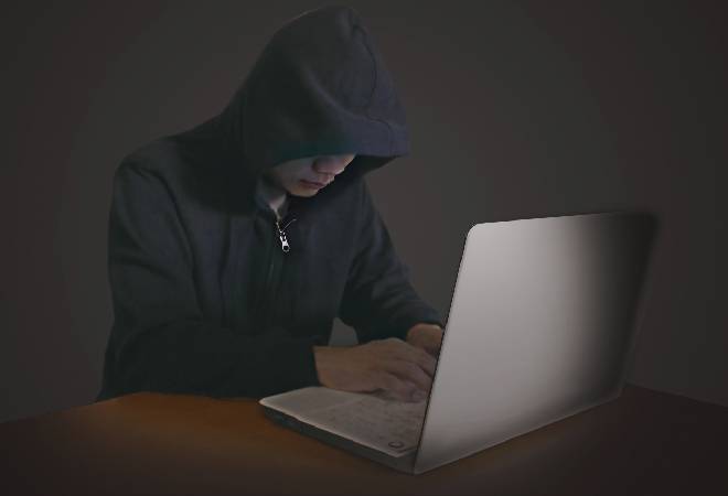 パソコンを操作するフードを被った男性。